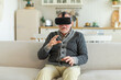 Excited mature senior man wearing using virtual reality metaverse VR glasses headset at home. Grandfather touching air during VR experience on virtual reality helmet. Simulation hi-tech videogame