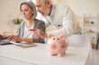 Pig money saving, piggy bank safe box close up, senior couple calculating, count total budget amount. Older adults learn how to interact with laptop online payment, finance, credit, transaction