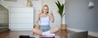 Healthy and fit fitness blogger, recording vlog for wellbeing social media account, sitting on yoga mat and showing thumbs up, using digital camera to create content, following script of laptop