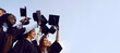 Group of happy multiethnic high school, college or university students having fun on graduation day and raising their graduate hats up to clear blue sky. Copy space banner background