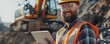 © amazingfotommm - The image depicts a construction worker in a reflective vest and hardhat using a tablet on a building site.