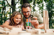 © Zamrznuti tonovi - Dad and daughter making tower of wooden blocks at picnic table.