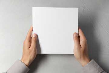 Canvas Print - Man holding blank book at light grey table, top view. Mockup for design