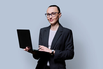 Middle-aged business confident woman using laptop on gray background