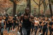 A muscular black man is teaching a fitness class outdoors in a park setting, with participants energetically following along on a vibrant morning