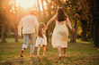 Young family of three are holding hands and running barefoot in park together at sunset.