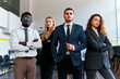 Confident multiethnic business team stands in modern office, poised for leadership. African, caucasian, arabic execs unite, exude corporate success, equity in work environment.