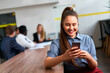 Smiling asian businesswoman in smart casual wear uses smartphone, team works at wooden table in modern office. Woman checks app, coworkers discuss project in blurred background, communication.