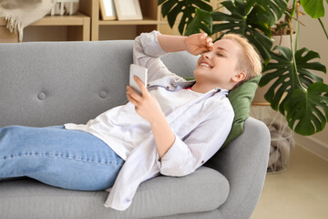 Poster - Young woman with short hair using mobile phone on sofa at home