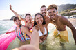 Portrait of a group of happy diverse young people in swimwear smiling and taking a selfie inside the water looking at the camera. Multiracial friends in the sea enjoying beach leisure and having fun