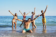 © CarlosBarquero - Portrait of a group of happy young people in swimming costumes posing for a photo on the shore of the beach. Diverse friends smiling and making playful gestures raising arms looking at camera
