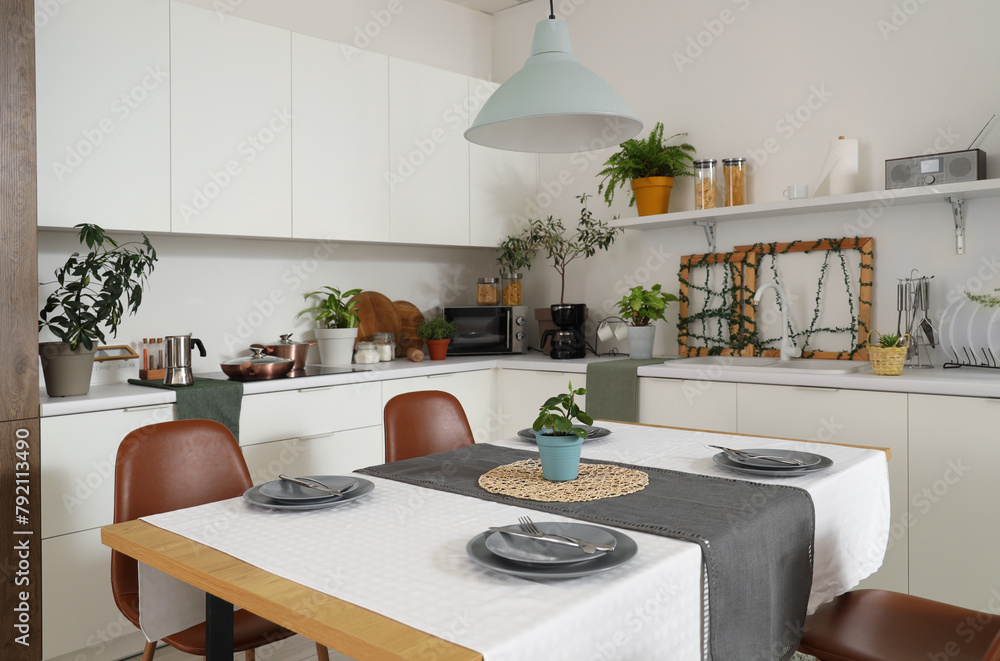 Interior of modern kitchen with green plants, dining table and counters