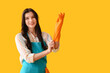Young woman putting on rubber gloves against yellow background