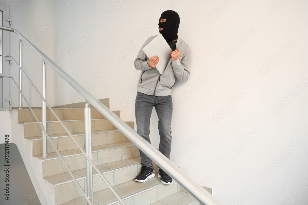 Male thief with laptop escaping in stairway