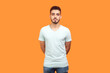 Portrait of serious handsome young bearded man wearing T-shirt standing looking at camera with bossy facial expression. Indoor studio shot isolated on orange background.