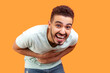 Portrait of happy joyful cheerful young bearded man wearing T-shirt laughing out loud holding belly hearing funny joke. Indoor studio shot isolated on orange background.