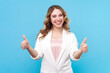 Portrait of satisfied delighted smiling blond woman with wavy hair showing like gesture positive feedback of service, wearing white shirt. Indoor studio shot isolated on blue background.