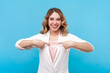 Portrait of happy joyful woman with wavy hair looking at camera with satisfied expression pointing at herself with delighted face wearing white shirt. Indoor studio shot isolated on blue background.