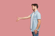 Side view portrait of smiling bearded man in blue casual style shirt standing makes greeting gesture stretches hand, meets with colleague. Indoor studio shot isolated on pink background.