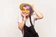 Portrait of astonished confused smiling woman with violet hair in sunglasses and hat looking with big surprised eyes good mood. Indoor studio shot isolated on white background.