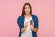 Portrait of sad unhappy shocked scared brown haired woman holding her comb with, loos hair, alopecia, wearing checkered shirt. Indoor studio shot isolated on pink background.