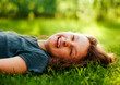 Happy laughing fun casual kid girl lying on the grass on nature summer sunny brigh background. Closeup