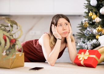 Wall Mural - Portrait of a saddened young woman at home against the background of a Christmas tree with presents