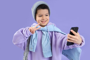 Sticker - Cute little Asian boy in adult clothes with mobile phone taking selfie on lilac background