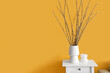 Vase with willow branches on table near yellow wall