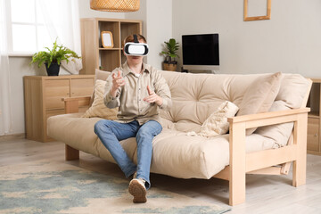 Wall Mural - Young man using VR glasses on sofa at home