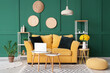 Stylish interior of green living room with yellow sofa, coffee tables, laptop and bouquet of narcissus flowers