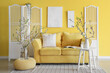 Stylish living room with yellow sofa, coffee table and vase with blooming branches