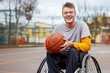 Determined and smiling disabled young man player in a wheelchair. Strong male boy smile at the camera sitting on a wheel chair alone in the basketball field with nobody playing in background