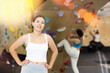 Smiling sporty young girl posing near climbing wall at bouldering gym after workout, feeling accomplished and energized