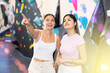 Two young women in sportswear posing against training wall at climbing wall