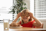 Fototapeta Kuchnia - Joyful girl with cookies over eyes, having a delightful snack time with milk and cookies. 