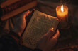 Close up of a prayer book held in hands with a candle flickering nearby