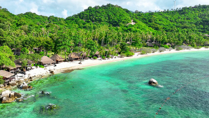 Discover a hidden gem on the green sandy shore, where the resort harmonizes with nature's beauty, offering a sanctuary by the sparkling sea. Drone aerial view. Tao island, Thailand. Beach background.
