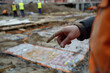 Close-up of an architect's hand pointing at specific details on a construction site, workers and materials in the background