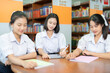 © Nutchapong Wuttisak - Three Asian female students are grouped together to work on a table with a laptop and several books to submit online work to a teacher in the library of a nationally famous school.