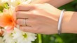 Womans wrist wearing a graceful silver bangle with delicate soft white lilies, set against a softfocus floral background