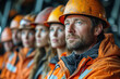 Group of factory workers in uniform and orange helmets.