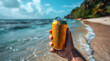 A hand holding up an unbranded yellow can of beer, with the ocean and blue sky in background