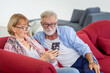 Senior couple using mobile smartphone in the living room, Man and a woman relaxing on a cozy sofa at home, Happy family concepts