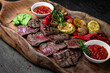  A large plateful of meaty cuts of mildly grilled steak with grilled vegetables. A set for a large company. Menu for a pub on a dark background. Colorful juicy food photography.