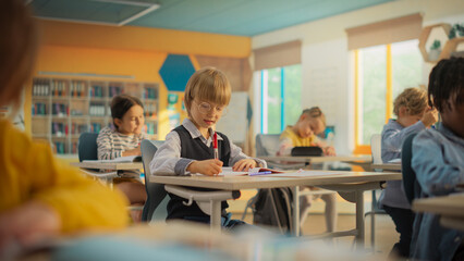 Wall Mural - Smart Little Boy Sitting Behind a Desk in Elementary School. Young Attentive Caucasian Man Writing Down Notes in Notebook, Finding a Solution to an Exercise