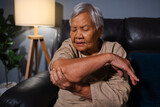 Fototapeta Lawenda - senior woman suffering from elbow pain while sitting on sofa in living room at night