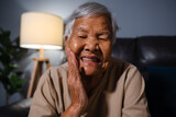 Fototapeta Lawenda - senior woman feels strong toothache while sitting on sofa in the living room at night
