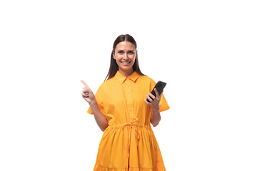 Wall Mural - pretty young brunette lady dressed in a bright yellow dress on vacation smiling joyfully holding a phone in her hand