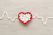 Cardiogram made with medicines and heart-shaped bowl on wooden background, top view